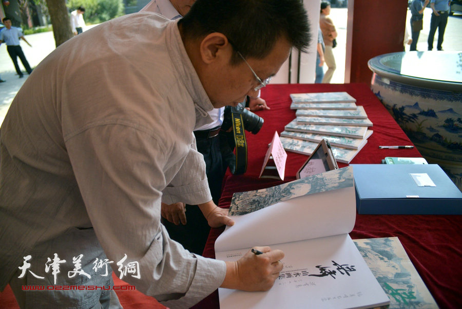 图为李毅峰为《梁崎先生精品山水画集》签名。