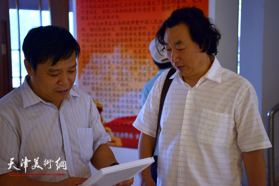 李耀春、韩石在阅读《南开区纪念抗日战争胜利七十周年书画展画集》。