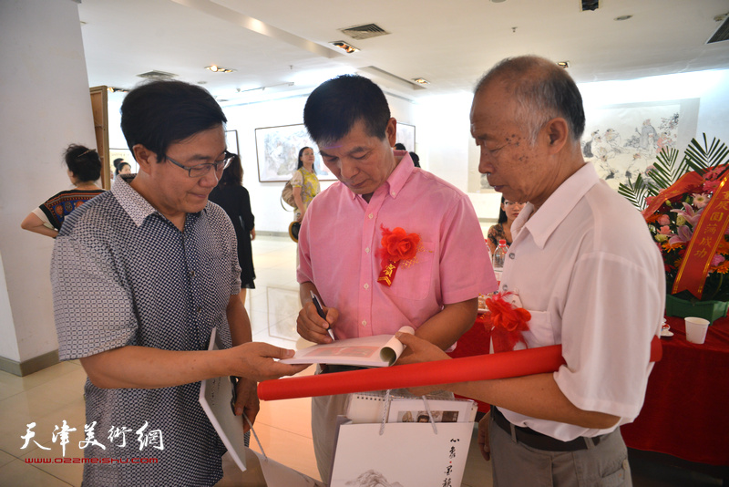 范扬为来宾在画展特刊《心象·墨韵—范扬人物画作品集》签名留念。