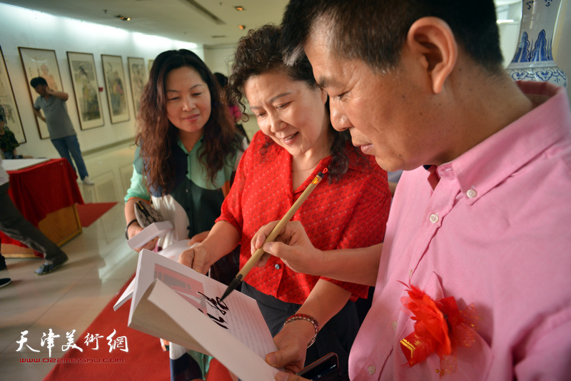 范扬为来宾在画展特刊《心象·墨韵—范扬人物画作品集》签名留念。