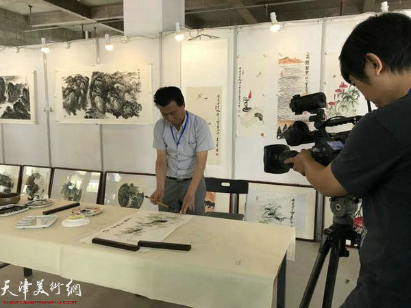 研究会理事、齐白石再传弟子李宝志先生在展览现场挥毫泼墨接受天津电视台国际频道记者采访