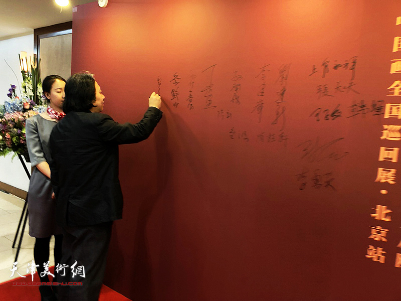 贾广健在画展背景墙上签名。