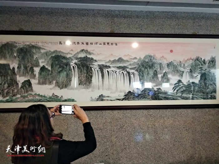 一位观众在欣赏马凤柏的山水画《旭日东升山河壮，碧水奔流万古长》，该画作已被澳门南光集团收藏。
