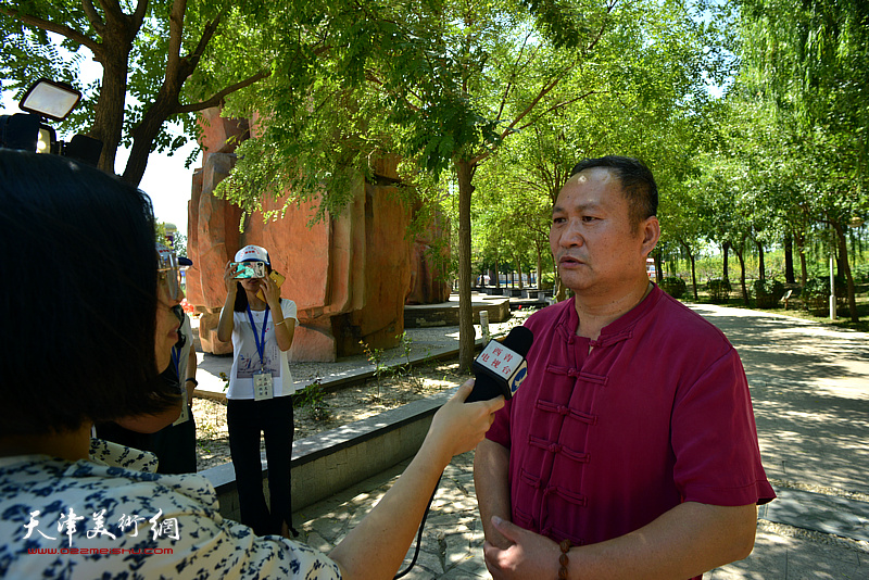 十月书画院院长陈子文在法治书画百米长卷展示现场接受媒体采访，介绍百米长卷的创作历程。