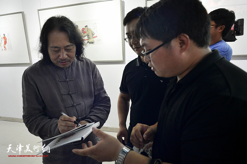 贾广健在画展现场观为观众签名留念。