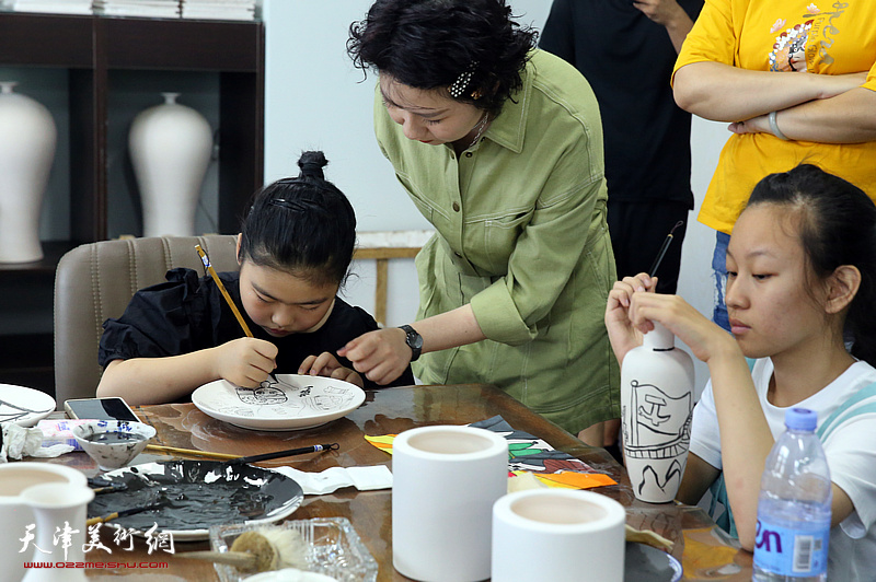 青年画家王霞在少儿瓷画创作体验活动现场指导孩子们画瓷。
