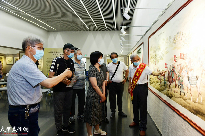 徐铁志向王青介绍展出的作品。